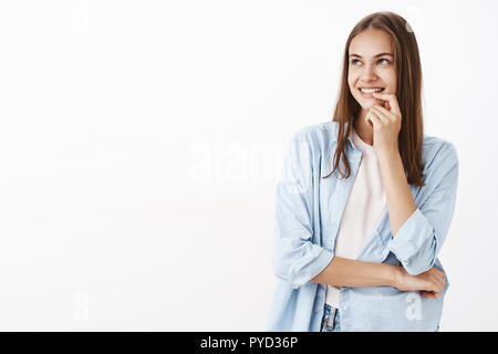 Mädchen eingedenk der erste Kuss mit Freund nostalgisch und flirty Blick auf die obere linke Ecke mit romantischen zufrieden und neugierig Lächeln holding Finger auf Lippe grinsend und Kreuzung Körper mit Arm Stockfoto