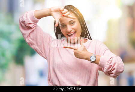 Junge geflochtenes Haar afrikanische amerikanische Mädchen mit Pullover über isolierte Hintergrund lächelnd, Rahmen mit Händen und Fingern, glückliches Gesicht. Creativ Stockfoto