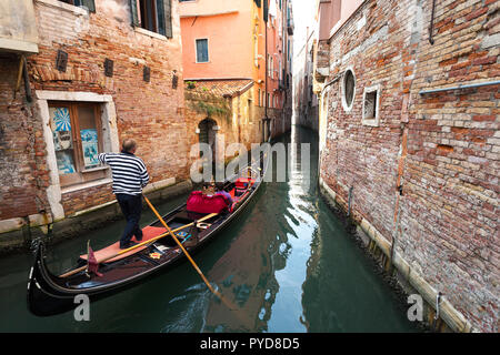 Venedig, Italien, Oktober 2018: Ein gondoliere navigiert seine Gondel mit Passagiere über einen engen Durchgang in Venedigs Kanäle Stockfoto