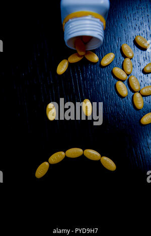 Traurige smiley mit gelben Pillen auf den Schwarzen Tisch Stockfoto