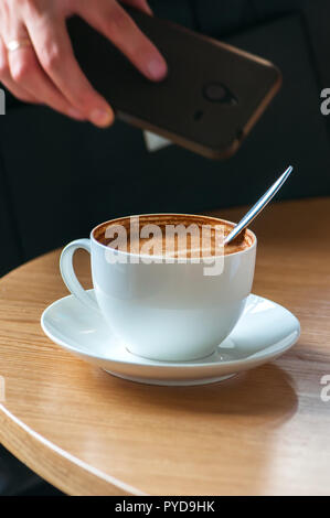 Nahaufnahme von Tasse Kaffee, Frau, ihr Smartphone auf hinterg Stockfoto