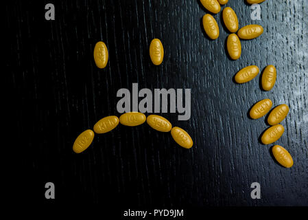 Traurige smiley mit gelben Pillen auf den Schwarzen Tisch Stockfoto