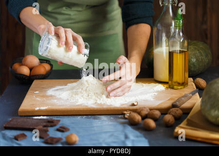 Hände kneten den Teig von Frauen. Konditoren Mehl im Teig. Auf einer hölzernen Tisch backen Zutaten Eier Kürbis Butter Milch Nüsse Nahaufnahme Stockfoto