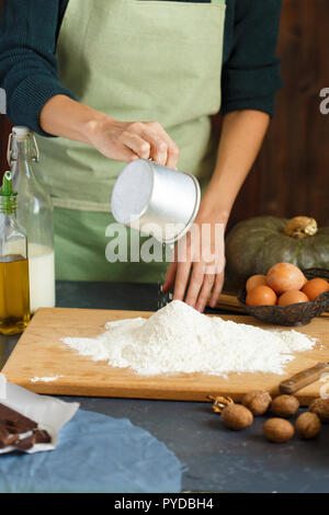Hände kneten den Teig von Frauen. Der konditor ist ein Ei in das Mehl. Auf dem hölzernen Tisch backen Zutaten. Kürbis Mehl Öl Milch C Stockfoto