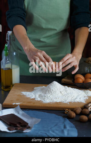 Hände kneten den Teig von Frauen. Der konditor ist ein Ei in das Mehl. Auf dem hölzernen Tisch backen Zutaten. Muttern Mehl Milch Kürbis Stockfoto