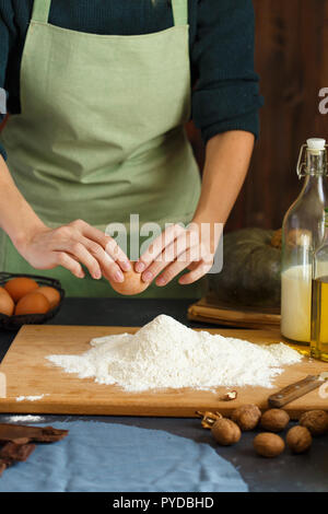 Hände kneten den Teig von Frauen. Der konditor ist ein Ei in das Mehl. Auf dem hölzernen Tisch backen Zutaten. Muttern Mehl Milch Kürbis Stockfoto