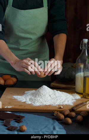 Hände kneten den Teig von Frauen. Der konditor ist ein Ei in das Mehl. Auf dem hölzernen Tisch backen Zutaten. Muttern Mehl Milch Kürbis Stockfoto