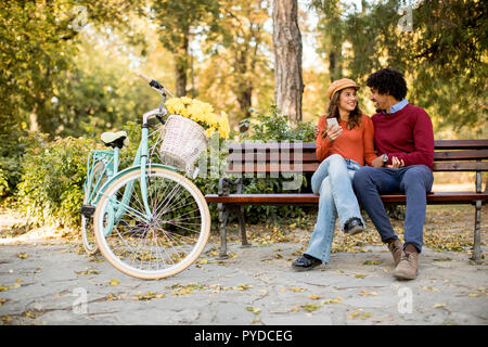 Multiratial Paar sitzt auf der Bank im Herbst City Park Stockfoto