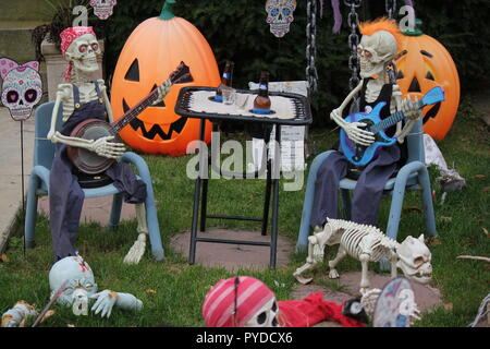 Zwei Musiker Skelette, ein Banjo und die anderen Spielen einer Gitarre, sitzen auf dem Rasen vor dem Haus, die Blockierung einer Melodie als kreative Halloween rasen Dekorationen. Stockfoto