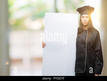 Junge hispanic Koch Frau Koch einheitliche Holding Banner mit einem selbstbewussten Ausdruck auf Smart Face denken Ernst Stockfoto