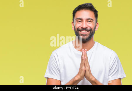 Nach Hispanic Mann über isolierte Hintergrund mit Händen gemeinsam beten um Vergebung bat lächelnd zuversichtlich. Stockfoto