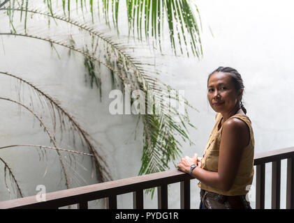 Asiatische Frau stehen auf Balkon mit weißen Wand und Baum hinter ihr Stockfoto