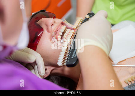 Frau in einer Zahnarztpraxis Auswahl Farbe ihrer Blätter. Zahnheilkunde und Gesundheitswesen Konzept. Zahnarzt mit Zahn Farbmuster auswählen Schatten für Patienten Zähne Zahnklinik. Zähne, die Konzept Stockfoto