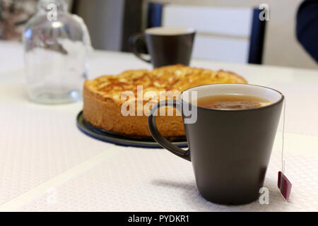 Eine heiße Tasse Tee mit hausgemachten Apfelkuchen. Dunkelgrau Teetasse mit einem Teebeutel und einem knusprigen Apfelkuchen im Hintergrund. Stockfoto