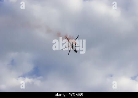 Kampfhubschrauber mit roten Rauch auf blauer Himmel mit weißen Wolken. Ansicht von unten. Stockfoto