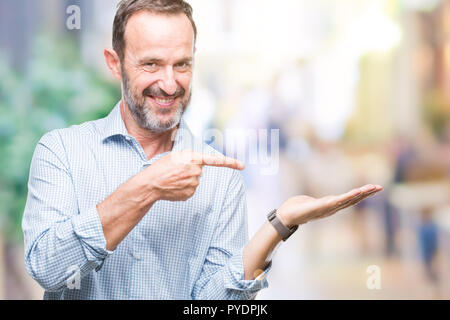 Mittleres Alter hoary Senior Business Mann über isolierte Hintergrund erstaunt und lächelt in die Kamera während der Präsentation mit Hand und zeigte mit dem Finger. Stockfoto