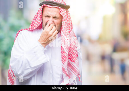 Senior arabischen Mann mit kufiya über isolierte Hintergrund riechen etwas stinkig und ekelhaft, unerträglichen Geruch, Atem mit dem Finger auf Stockfoto