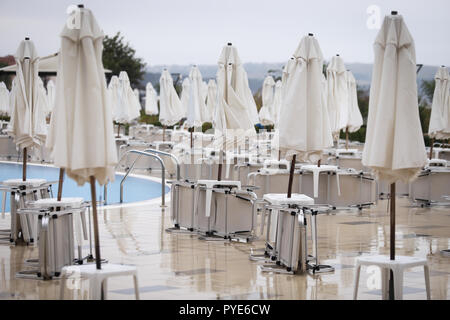 Geschlossen mit Sonnenschirmen und Liegestühlen, die um einen Pool in der Nebensaison, mit keine Personen, die in einem kalten bewölkten Tag, im späten Herbst auf der bulgarischen Küste Stockfoto