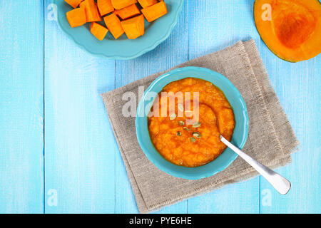 Kürbispüree in einem blauen Platte auf einer hölzernen blauen Tabelle. Kürbisscheiben auf dem Tisch. Ansicht von oben. Kopieren Sie Platz. Stockfoto