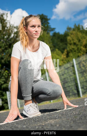 Eine junge Frau in Sportswear ist kniend an den Start vorbereiten, die Run Stockfoto