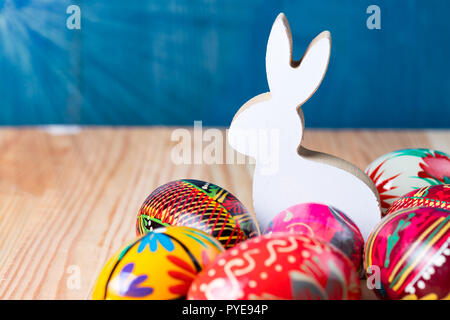 Osterhase Figur mit bunten Eiern auf natürliche Holz- Hintergrund. Kopieren Sie Platz auf der linken Seite. Warmes Sonnenlicht Flare. Stockfoto