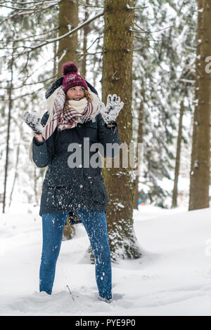 Eine junge Frau hat Spaß in einer winterlichen Wald und hält einen Schneeball in Ihrer Hand Stockfoto