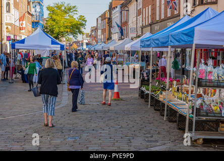Open air Marktplatz im Stadtzentrum von Chichester in West Sussex mit Verkaufsständen entlang der Straße in der Nähe der Kathedrale und des Kreuzes. Stockfoto