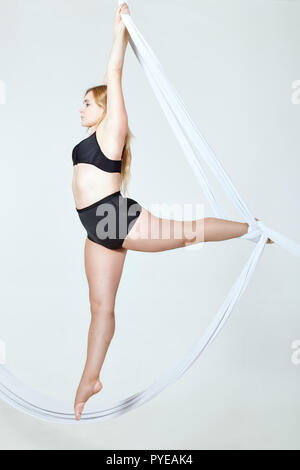 Junge blonde Frau im schwarzen Badeanzug die Tricks auf Leinwand auf weißem Hintergrund. Stockfoto
