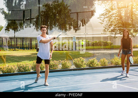 Hübscher junger Mann stand am Tennisplatz und Tennis spielen, während die hübsche junge Frau sieht ihn an. Stockfoto