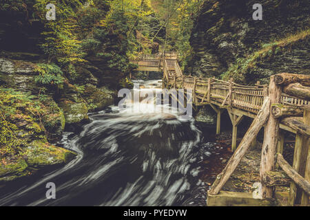 Fußgängerbrücke Kurven um die Schluchten von Bushkill Falls in Poconos, PA, umgeben von üppigen Herbst Laub Stockfoto