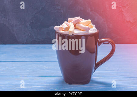 Braun Keramik Becher voller Marshmallows und heiße Schokolade auf einem blauen Hintergrund aus Holz Stockfoto