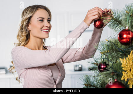 Lächelnd attraktives Mädchen schmücken Weihnachtsbaum mit Spielereien zu Hause Stockfoto