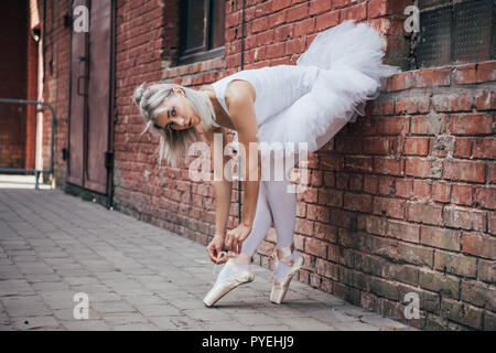 Schöne junge Ballerina lehnte an der Wand und Binden pointe Shoe Stockfoto