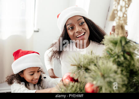 Portrait von Happy afrikanische amerikanische Familie in Santa Claus Hüte Dekoration Weihnachtsbaum gemeinsam zu Hause Stockfoto