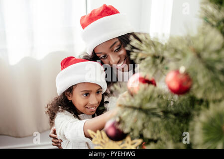 Portrait von Happy afrikanische amerikanische Familie in Santa Claus Hüte Dekoration Weihnachtsbaum gemeinsam zu Hause Stockfoto