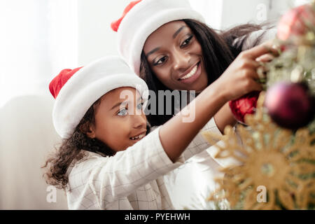 Afrikanische amerikanische Mutter und Tochter in Santa Claus Hüte Dekoration Weihnachten Baum zusammen zu Hause Stockfoto