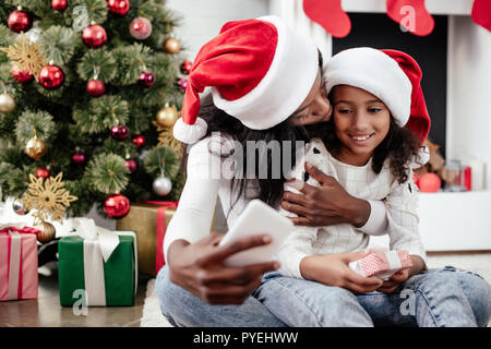 Afrikanische amerikanische Familie in Santa Claus Hüte unter selfie auf dem Smartphone in eingerichtete Zimmer zu Hause, Weihnachten Konzept Stockfoto