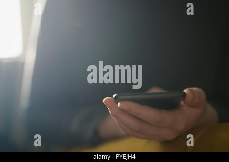 Closeup junge weibliche mit Smartphone sitzt zuhause in der Nähe von Fenster, flacher Fokus Stockfoto