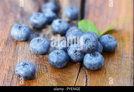 Blaubeeren mit grünen Blättern auf einem alten Holztisch Stockfoto