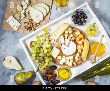 Verschiedene Arten von Käse auf Holzbrett, Oliven, Obst-, Mandel- und Weingläser auf Weiß fach Ansicht von Oben Stockfoto