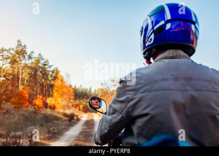 Ältere Menschen reiten Roller auf autumn forest road. Treiber im Helm reiten Moped. Ansicht von hinten Stockfoto