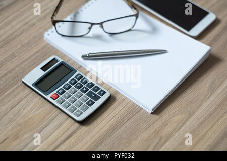 Notepad, Calculator, Smartphone, Gläser und Splitter Kugelschreiber auf Holz Büro Schreibtisch. Selektive konzentrieren. Stockfoto