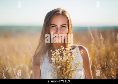 Attraktive junge Frau, die lächelnd auf der Wiese in ärmelloses Jean sundress in Kamera suchen Stockfoto