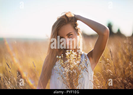 Attraktive junge Frau, die in der Wiese in ärmelloses Jean sundress reichte ihr langes Haar. Stockfoto