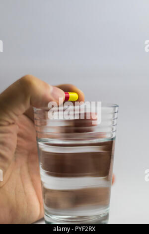 Männer gibt einen roten und gelben Pille in ein Glas Wasser, Medizin Stockfoto