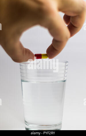 Männer gibt einen roten und gelben Pille in ein Glas Wasser, Medizin Stockfoto