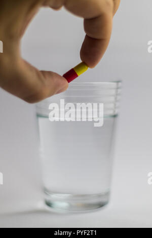 Männer gibt einen roten und gelben Pille in ein Glas Wasser, Medizin Stockfoto