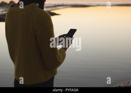 Eine Frau mit Handy am Strand bei Sonnenuntergang Stockfoto