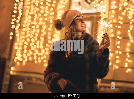 Schöne Mädchen, dass eine Wunderkerze genießt weihnachtliche Stimmung in alten Europäischen Stadt auf festliche Goldgelb leuchten bokeh Hintergrund Stockfoto