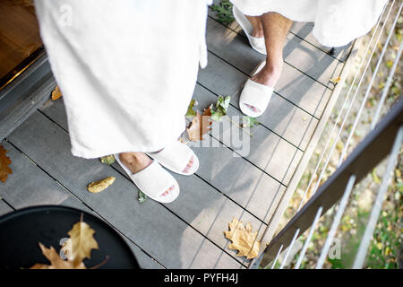 Paar in Bademantel und slipppers stehen auf der Terrasse mit schönen Blätter im Freien. Sicht von oben mit kein Gesicht Stockfoto